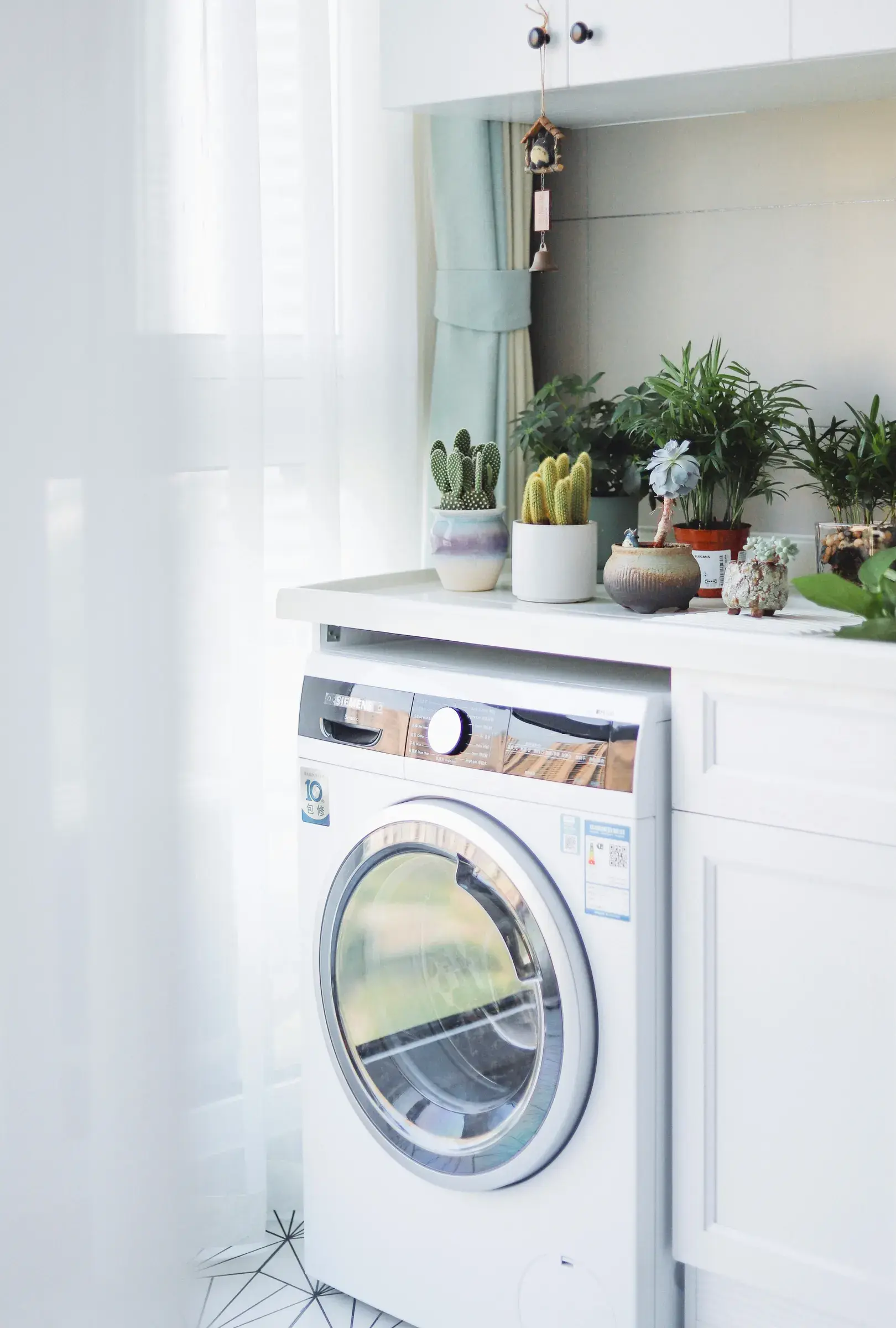 A front-loading washing machine installed in a bright utility room beside a window